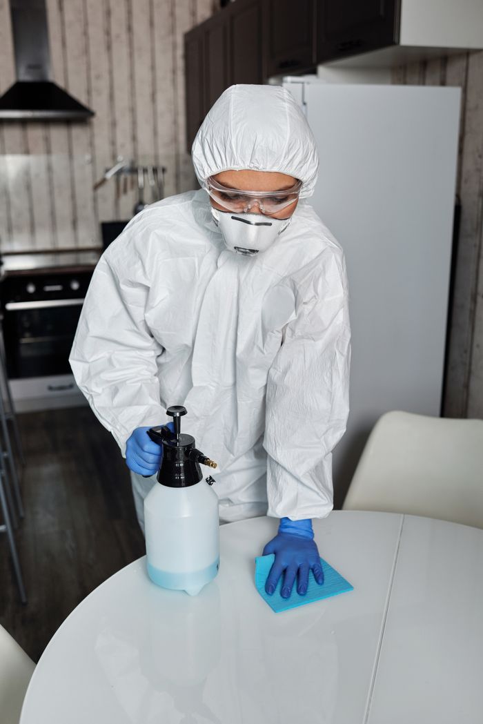 services-02 A person in full PPE disinfecting a table indoors for hygiene and safety.